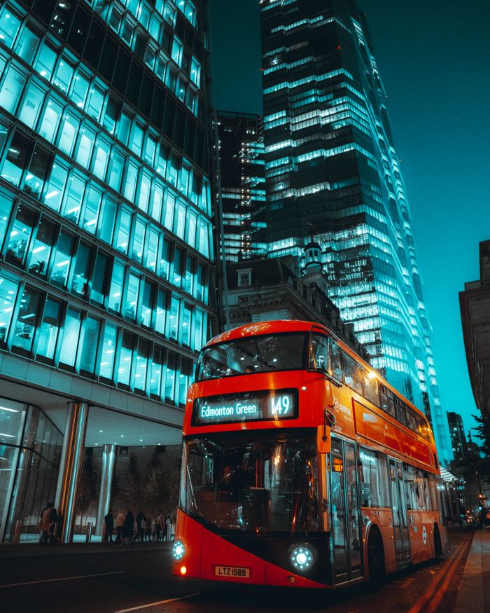 Stunning London cityscape featuring illuminated skyscrapers and a classic red double-decker bus at night.